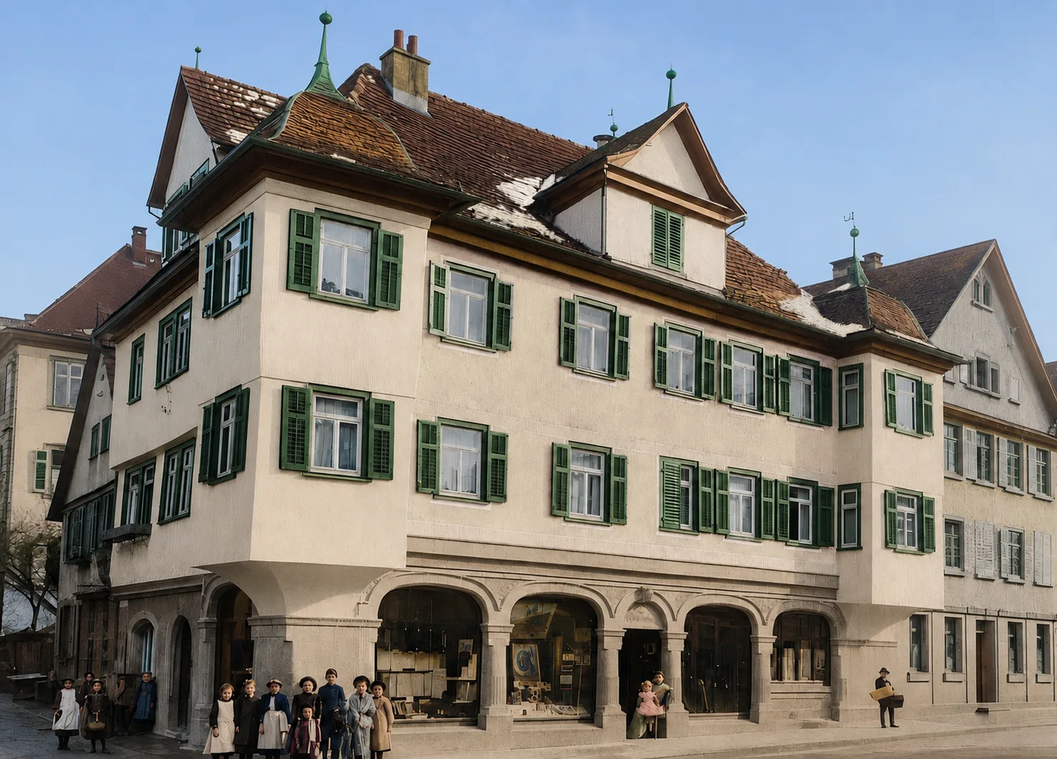 Das Ladengeschäft von Münch Mode im Jahr 1906: ein Eckhaus mit Arkadengang, grünen Fensterläden und Schaufenstern im Erdgeschoss. Davor stehen vierzehn Kinder und ein Mann mit einem Koffer.